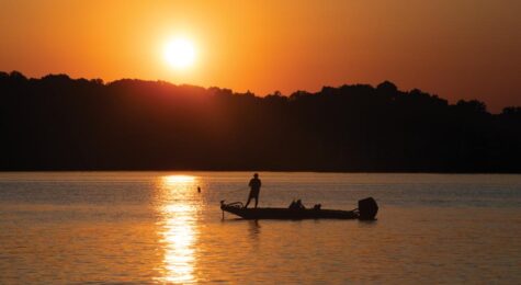 A fisherman on a boat as the sun sets as viewed from Louisville Point Park in Louisville.