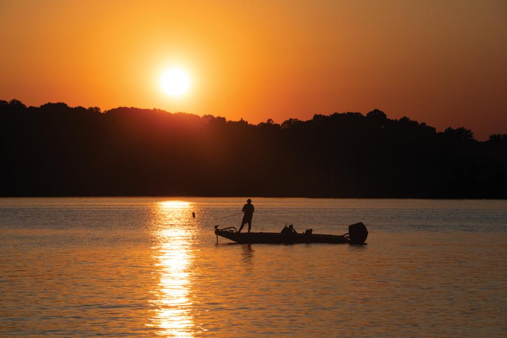 A fisherman on a boat as the sun sets as viewed from Louisville Point Park in Louisville.