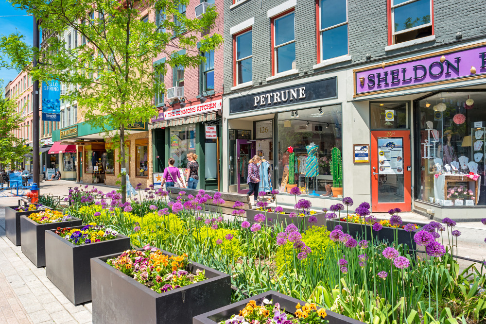 People walk past colorful stores in a pedestrian area of downtown Ithaca, New York, on a sunny day. Ithaca is a best city in New York.