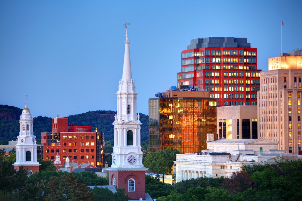 A church steeple in the foreground of downtown New Haven, CT, at sunset. New Haven is a top city to live in Connecticut.