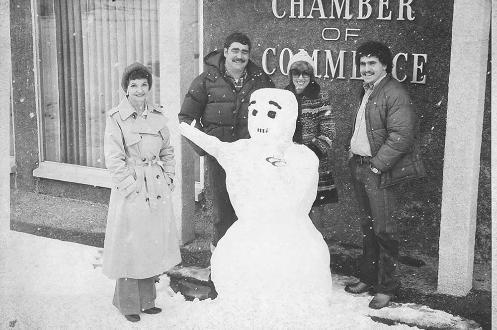 Oak Ridge Chamber of Commerce staff stands outside of their building with a snowman during a snowy day in Oak Ridge, TN.
