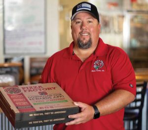 CJ Eversole, owner of Pizza Factory, poses with a pizza box.