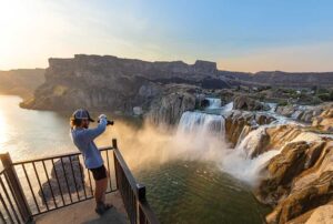 Man takes a photo of the view on an overlook at Shoshone Falls at sunset in Twin Falls, Idaho.