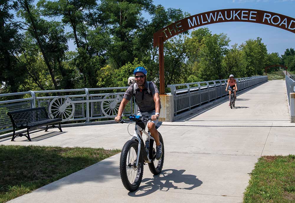 Man rides a bike with a dog in his backpack along the Marion Dual Bridge, which is located along the Grant Wood Trail in the Cedar Rapids, IA, area.