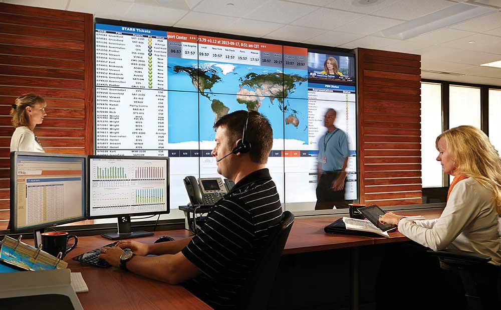 Employees at the Rockwell Customer Service Center for Collins Aerospace work in front of a big screen.