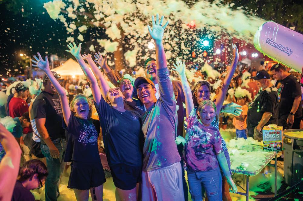 Foam Dance Party! A sea of smiling faces, bathed in neon lights, disappears into a mountain of foam. The energy is electric as the beat drops and the dance floor erupts.
