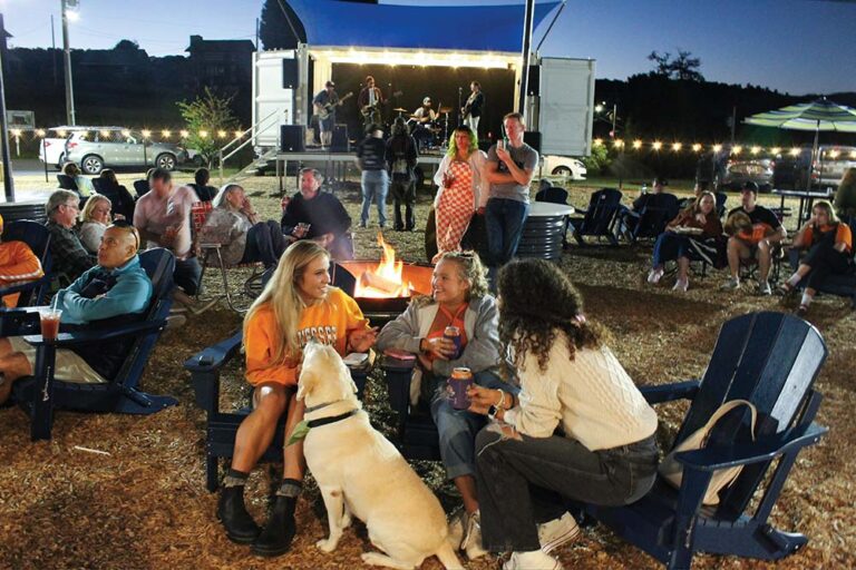 People gather around fire pits enjoying drinks and socializing with their dogs at Off Leash Social in Johnson City, TN.