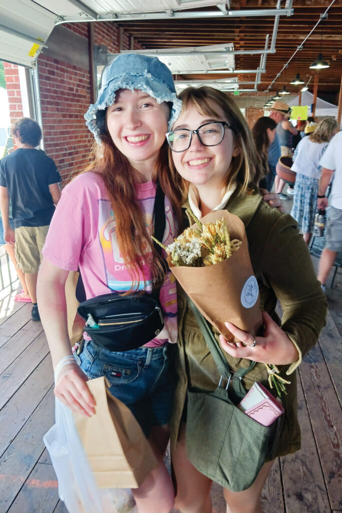 Two young women pose with their purchases at Nampa Farmers Market.