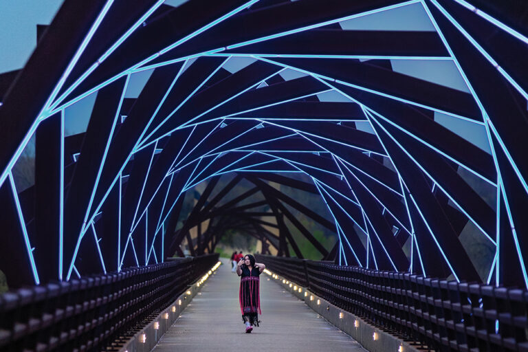 A woman takes a selfie while walking across the High Trestle Trail Bridge in Madrid, Iowa. The bridge lights up in blue at night.