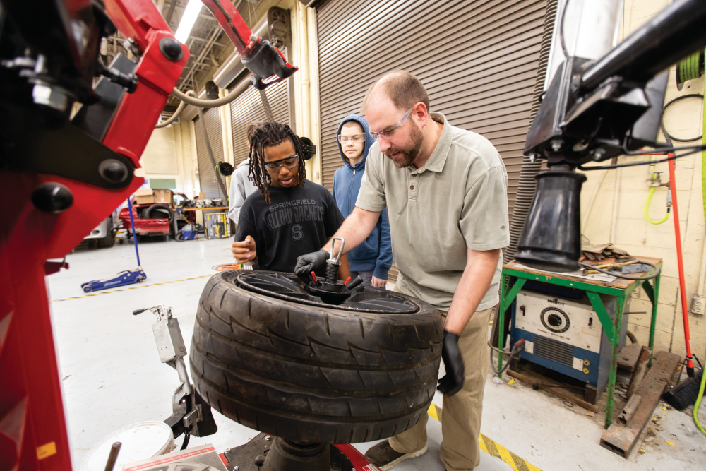 Instructor Daniel White shows Kemarious Taylor how to remove a cars tire from a rim in an automotive that is part of Springfield High School's Career and Technical Education program.