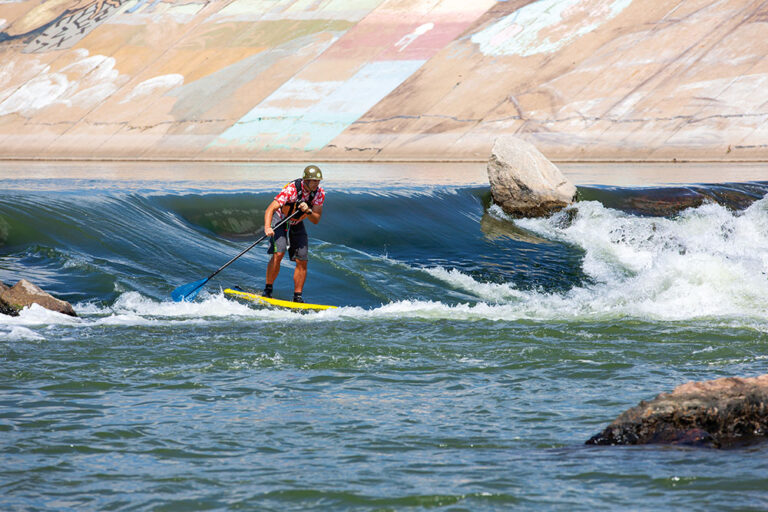 A man rides down a rapid on a paddle board at Whitewater Park in Pueblo, CO.