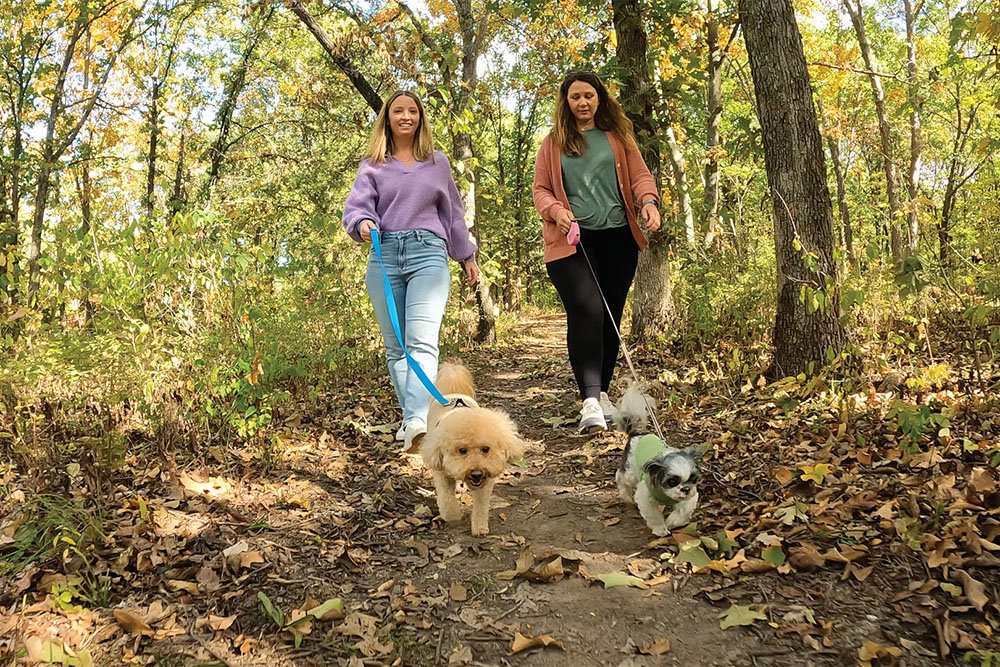 Two women walk their dogs along a trail at the Overland Park Arboretum & Botanical Gardens.