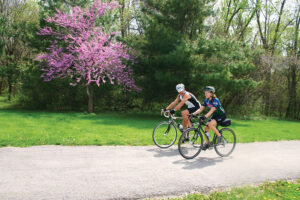 A man and a woman ride their bikes on a paved trail in Overland Park, KS, in spring.