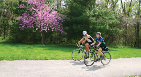 A man and a woman ride their bikes on a paved trail in Overland Park, KS, in spring.