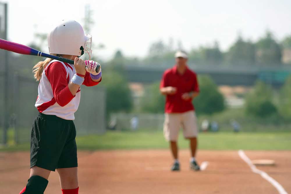 This is an image of a father coaching his daughter at a girls softball game. She's in focus with a relatively shallow depth of field. He's lens blurred but you can imagine him motioning with his hands.