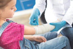 Doctor in white coat and medical gloves bandaging hand of little girl