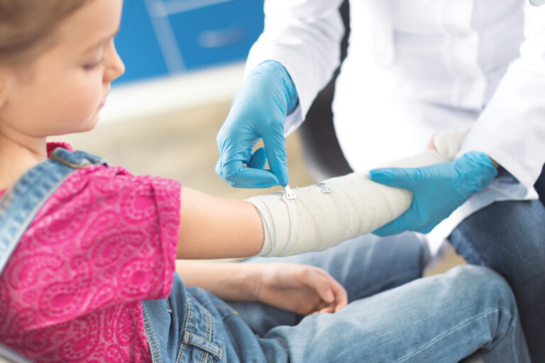 Doctor in white coat and medical gloves bandaging hand of little girl