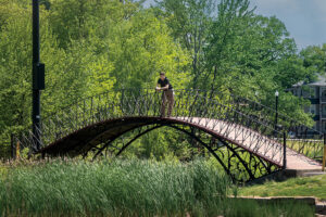 A man pauses to enjoy the scenery from a curved bridge at Elm Park in Worcester, MA.