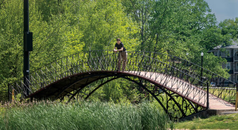 A man pauses to enjoy the scenery from a curved bridge at Elm Park in Worcester, MA.