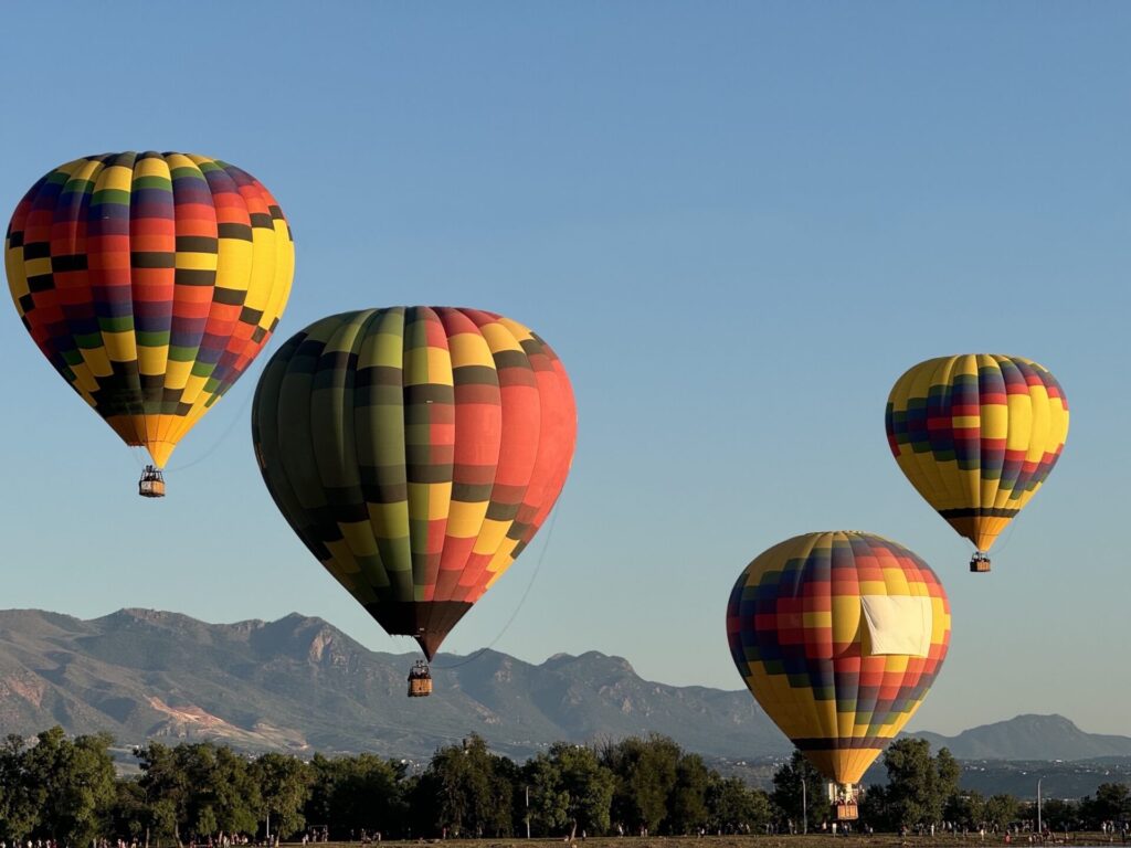 Four vividly colored hot air balloons float agains a backdrop of mountains in Colorado Springs, CO. Colorado Springs is a top family vacation destination in Colorado.