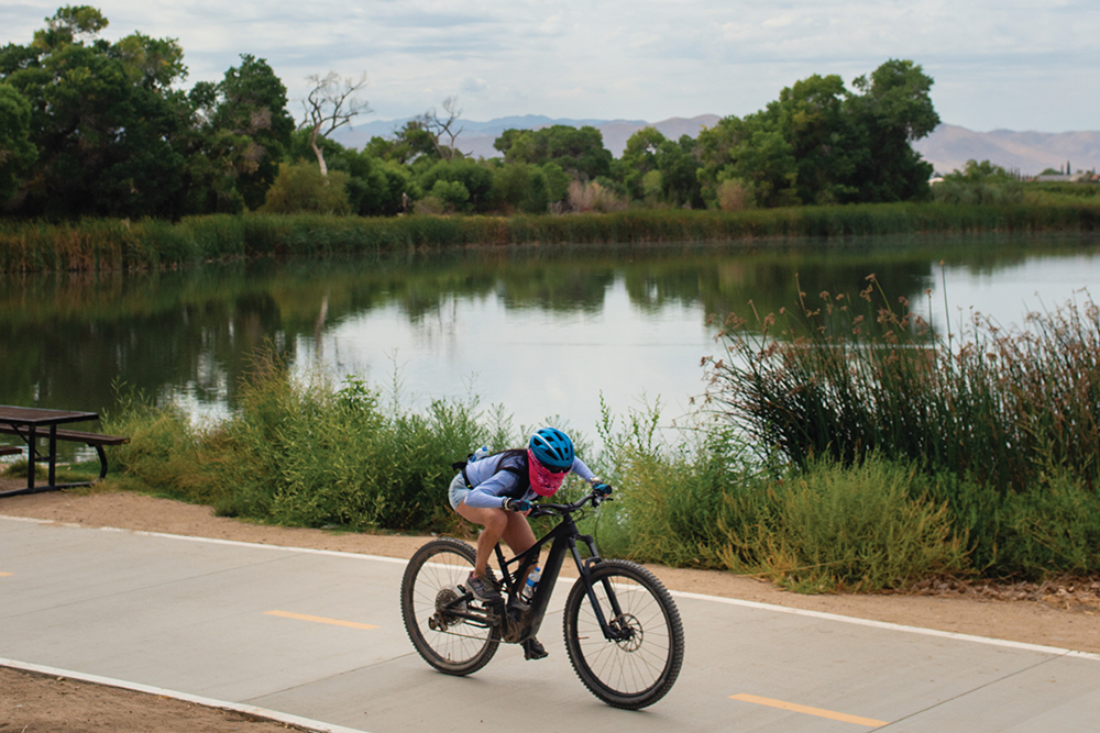 A woman rides her bicycle along the river on the Mojave River Walk in the Mojave Narrows Regional Park in Victorville, CA.