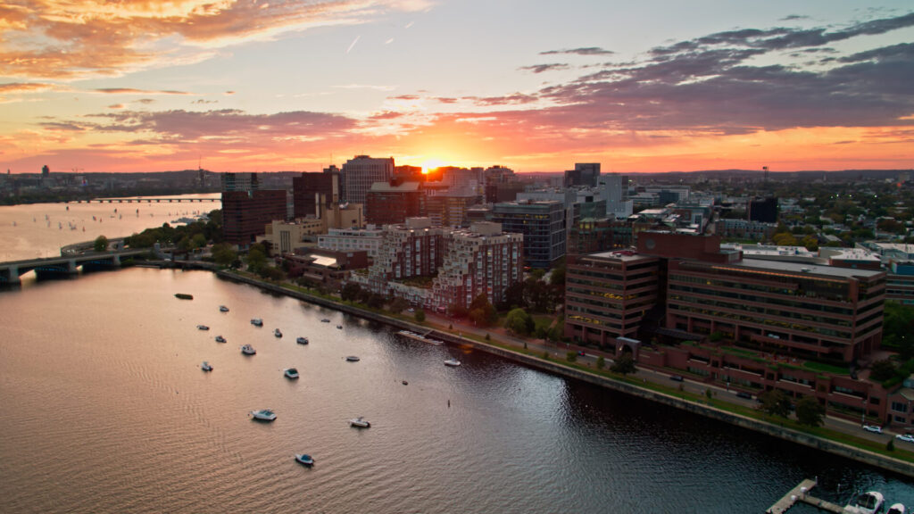 Aerial shot of Cambridge, Massachusetts at sunset on an evening in early Fall, taken from over the Charles River and looking down on offices and apartment buildings on the waterfront.