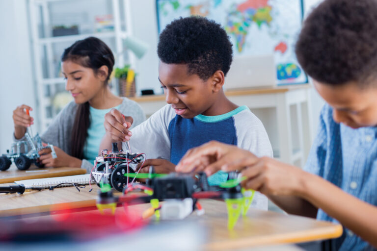 Happy middle school students work on projects during after school robotics club. They are building robotic vehicles and drones.