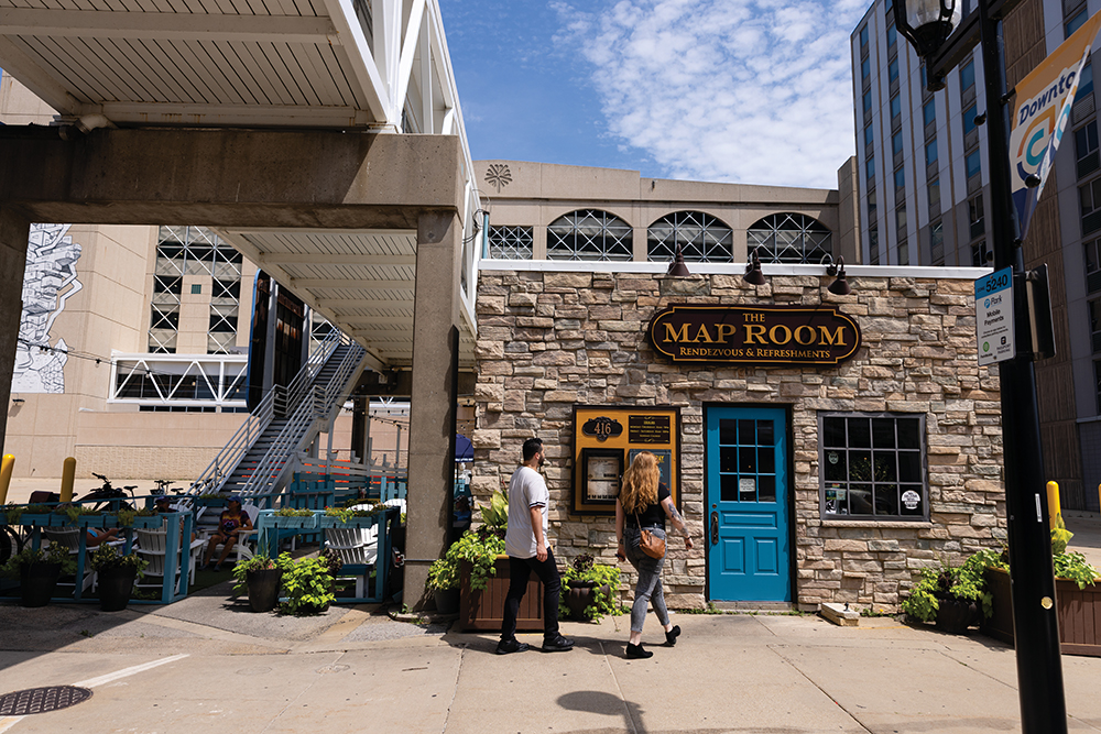 A couple walks into The Map Room restaurant, which is nestled under an overpass and towering parking garage in a tiny stone building that’s been its home for almost a century.