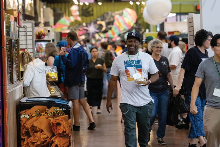 A man walks through the crowded NewBo City Market with his food purchase.