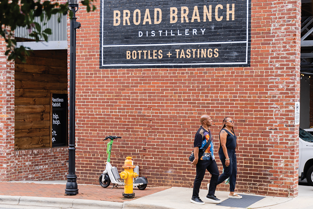 People walk past the brick exterior of Broad Branch Distillery in Winston-Salem, NC.