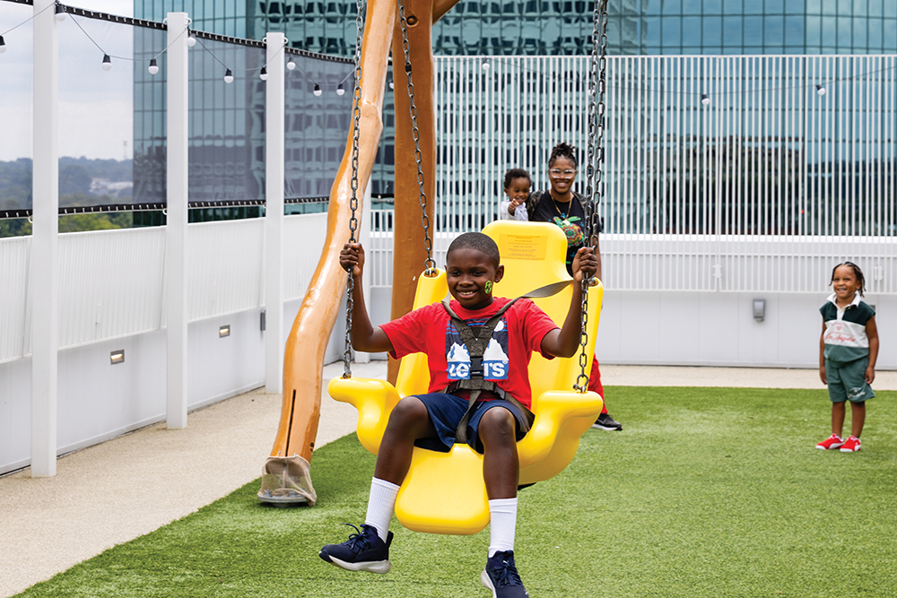 A boy swings in the rooftop adventure area at Kaleideum in Winston-Salem, NC, while his family looks on.