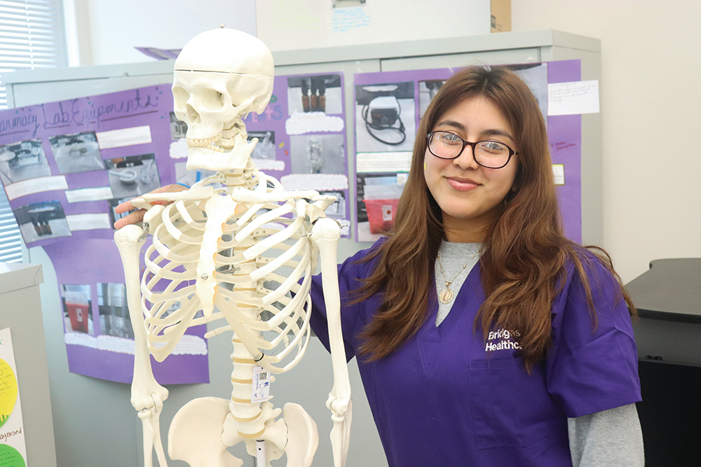 A female Winston-Salem/Forsyth County Schools student poses with a skeleton for a photo.