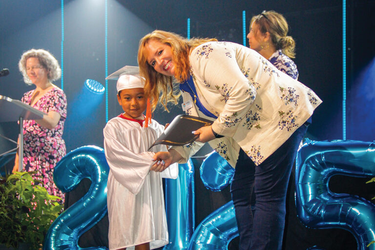 A woman shakes the hand of a young child wearing a cap and gown.