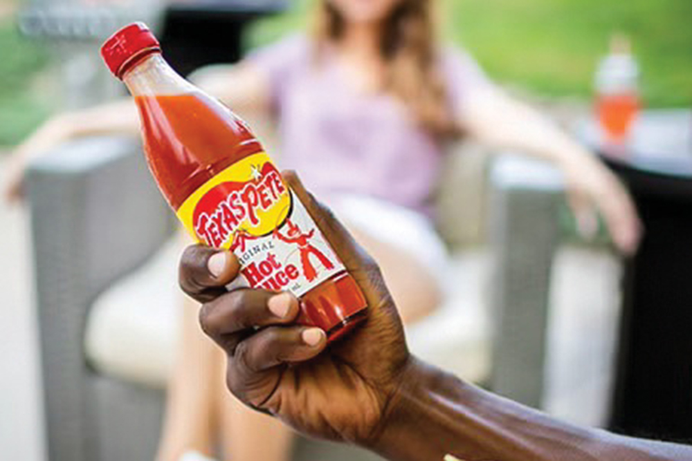 Closeup of a man holding a bottle of Texas Pete Original Hot Sauce in his hand. The hot sauce is made by Garner Foods, based in Winston-Salem, NC.