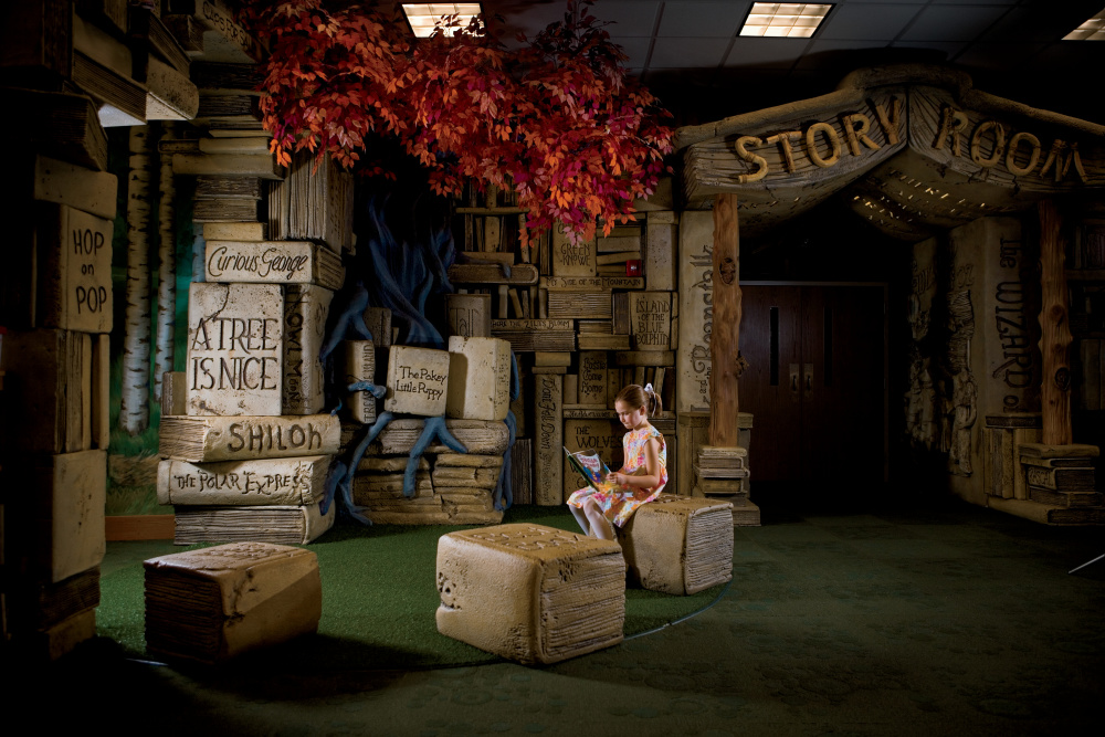 Lilly reads a book in the Brentwood Library's children area which has a display of oversized books and a tree designed by Artisan Industries in Maury County.
