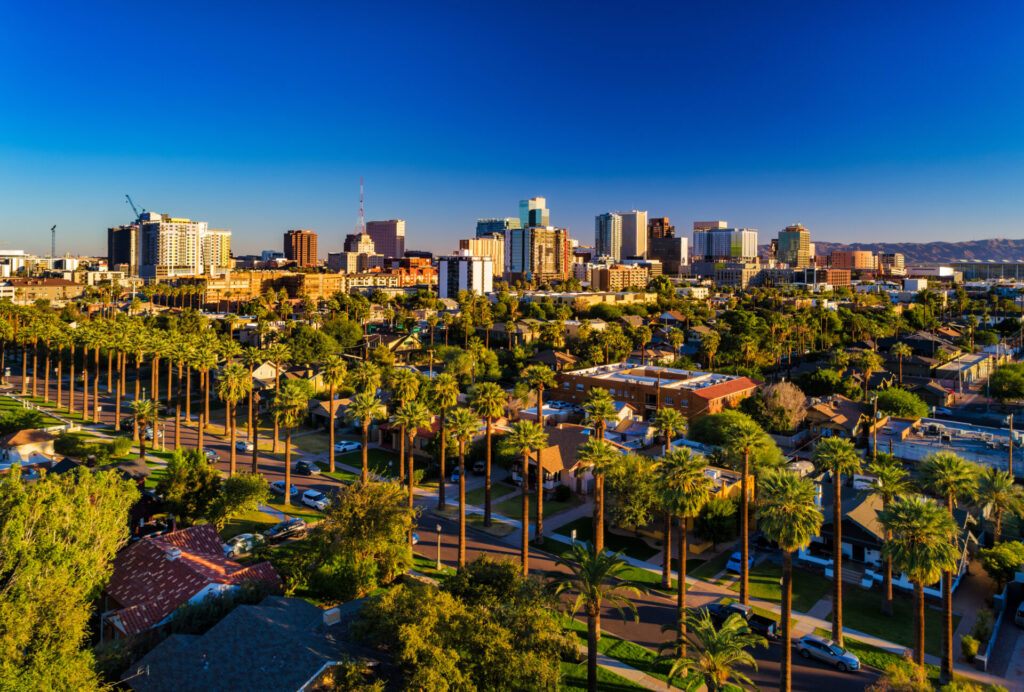 Aerial of Downtown Phoenix skyline with a residential neighborhood with many palm trees in the foreground.