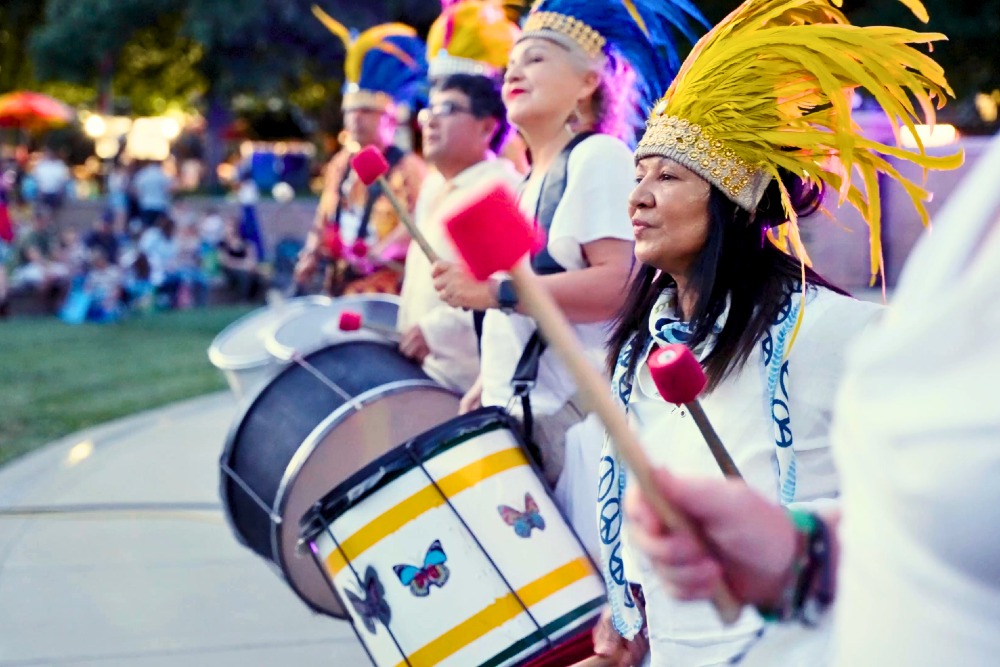 A group of Native Americans in colorful headdresses play traditional music on drums in Rancho Cordova, CA.