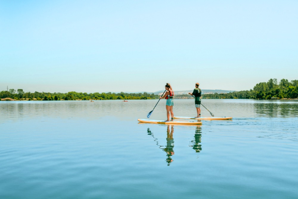 A man and a woman paddle board on a lake in Rancho Cordova, CA. Plentiful outdoor activities are one of the perks of living in Rancho Cordova.