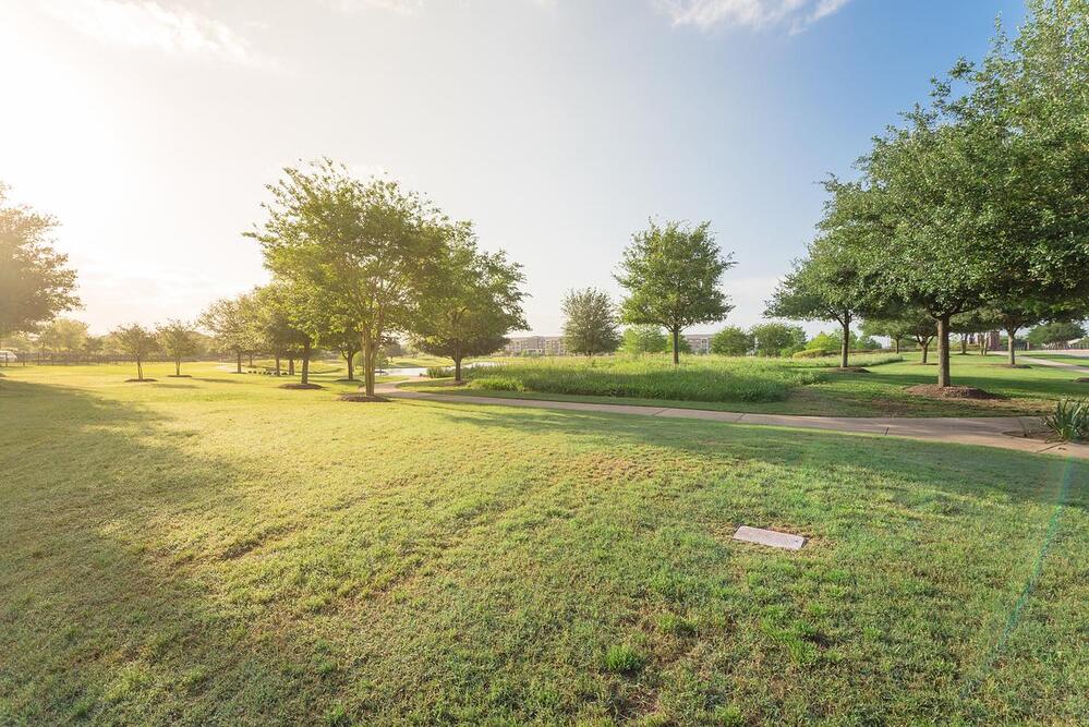 A panorama view of an urban park in Sugarland, Texas, features a green grass lawn, oak trees and walking/biking path illuminated by sunshine during early spring morning.