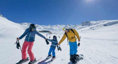 Family skis groomed ski run on sunny day, Val Thorens