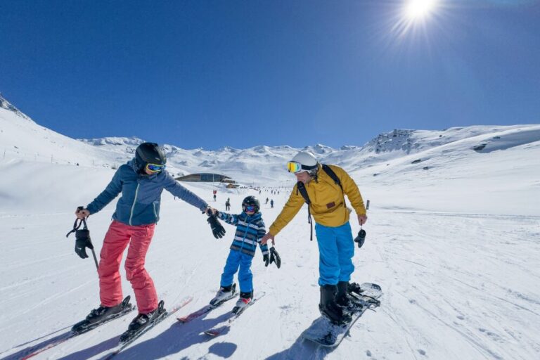 Family skis groomed ski run on sunny day, Val Thorens