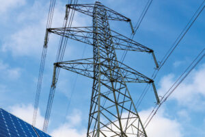 Solar panels and electricity pylon against blue sky.