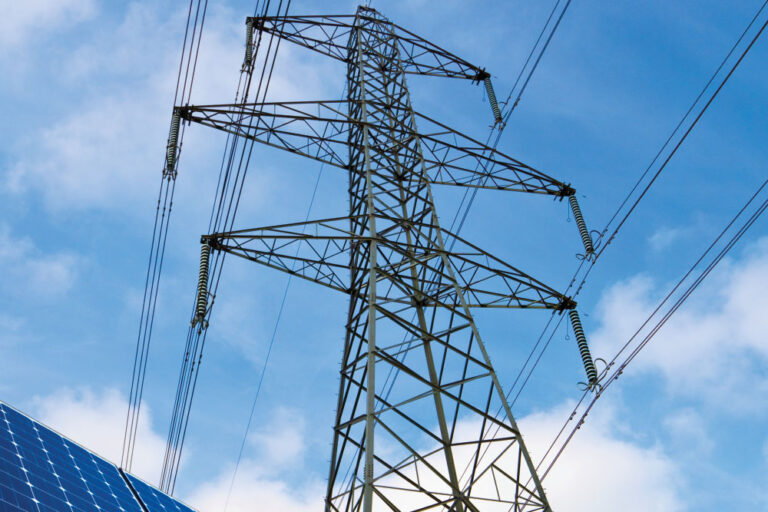 Solar panels and electricity pylon against blue sky.