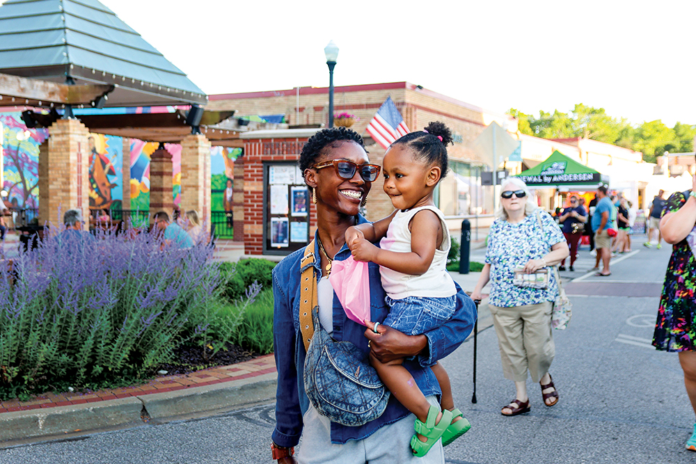 A mom carries her toddler through the street at the Downtown OP Art Fair in Overland Park, KS.
