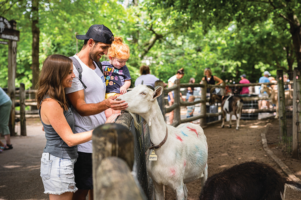 A couple and their small child pet a goat at the Deanna Rose Children's Farmstead in Overland Park, KS.