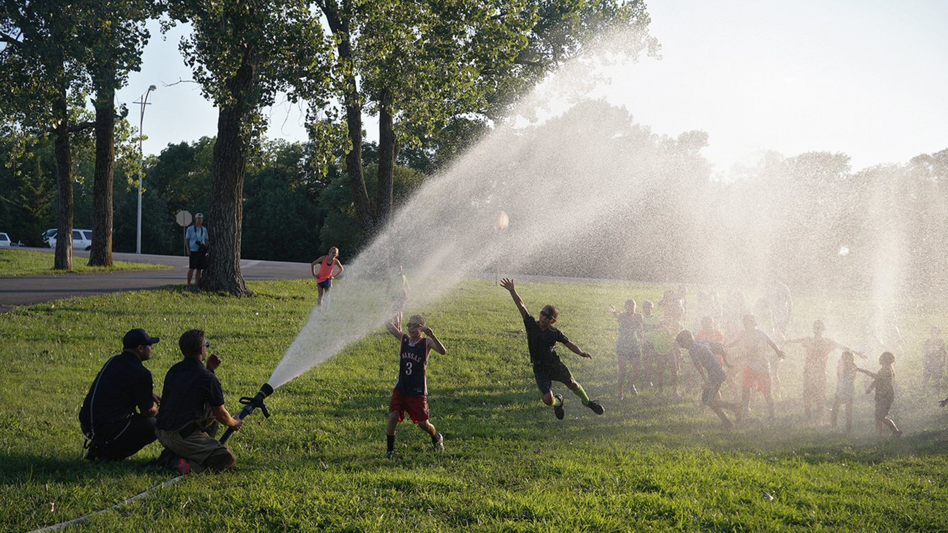 A scenic shot of a water spray in the park and kids playing under it in Lenexa, Kansas.