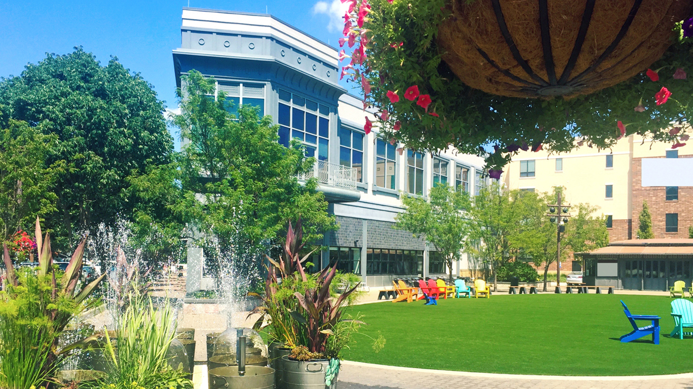 A retail district with a green lawn dotted with colorful Adirondack chairs.