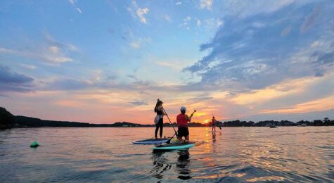 People paddleboard on the water at sunset.