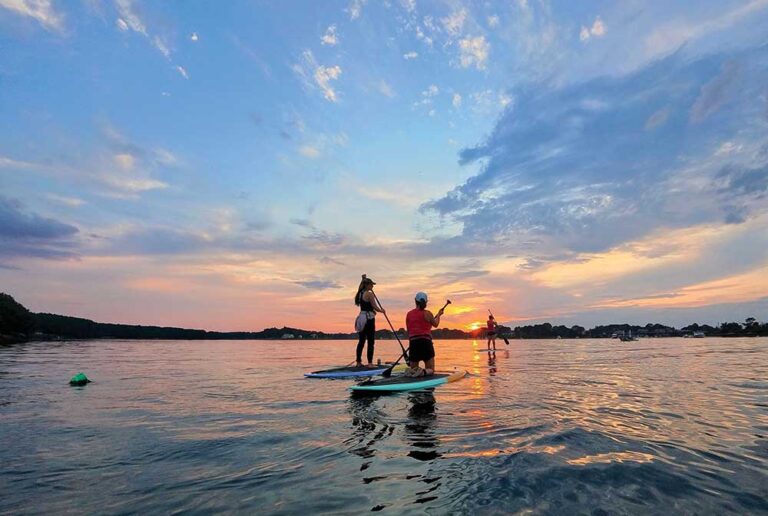 People paddleboard on the water at sunset.