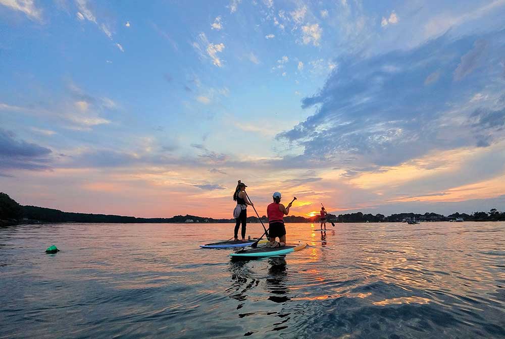 People paddleboard on the water at sunset.